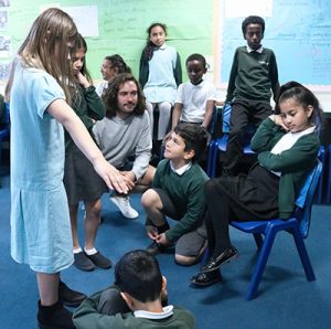 Children role playing in a classroom, with Joe Wicks looking on