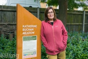 woman leaning against Katherine Buchan meadow sign, in the Hanwell meadow
