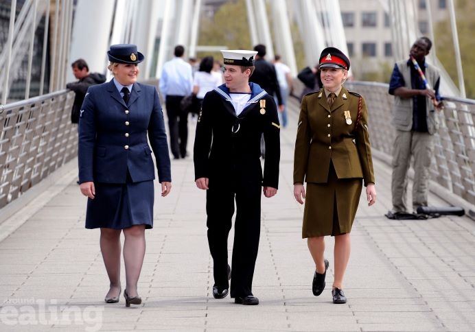 Three people walking side by side across a bridge, smiling and chatting. The first woman on the left is dressed in a Royal Air Force uniform, the person in middle is in a Navy sailor's uniform and the woman on the far right is wearing a smart Army uniform with jacket, skirt and hat.