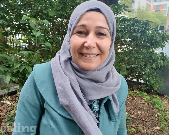 Picture of refugee Layla Othman smiling and standing outside wearing headscarf and green coat