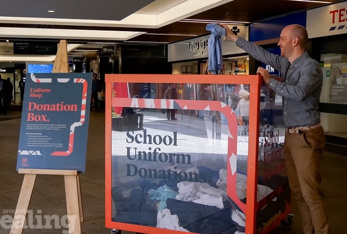 Large plastic box with School Uniform Donations written across the front - a man dropping a piece of school uniform into the box