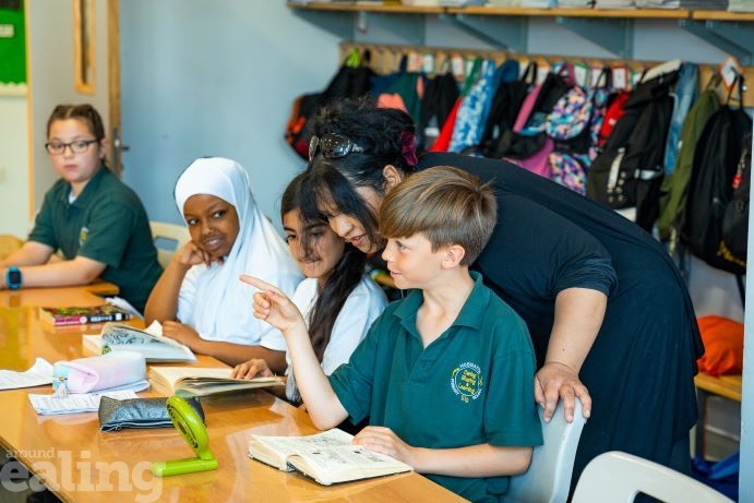 3 pupils sitting in a row and teacher leaning over boy's shoulder