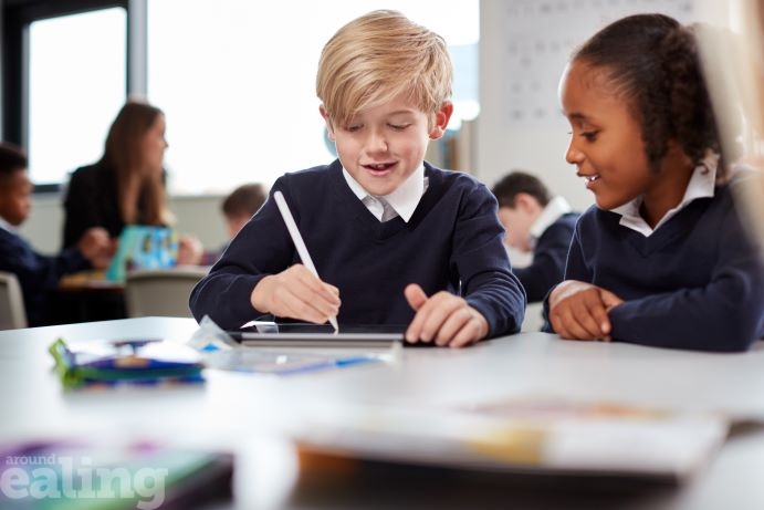 young male pupil writing at a desk in classroom, sitting next to young female classmate