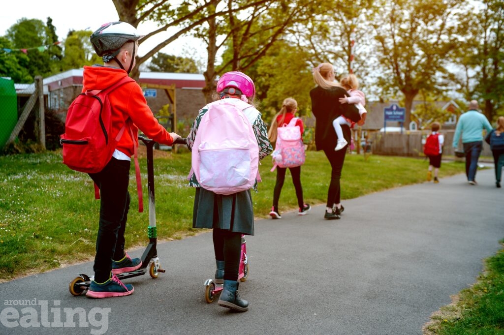 a woman carrying a child in front of children scooting on the pavement