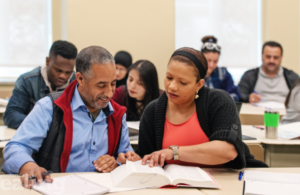 Two adult learners sit and read text book in class