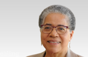 Woman with short grey hair wearing red glasses smiles at camera