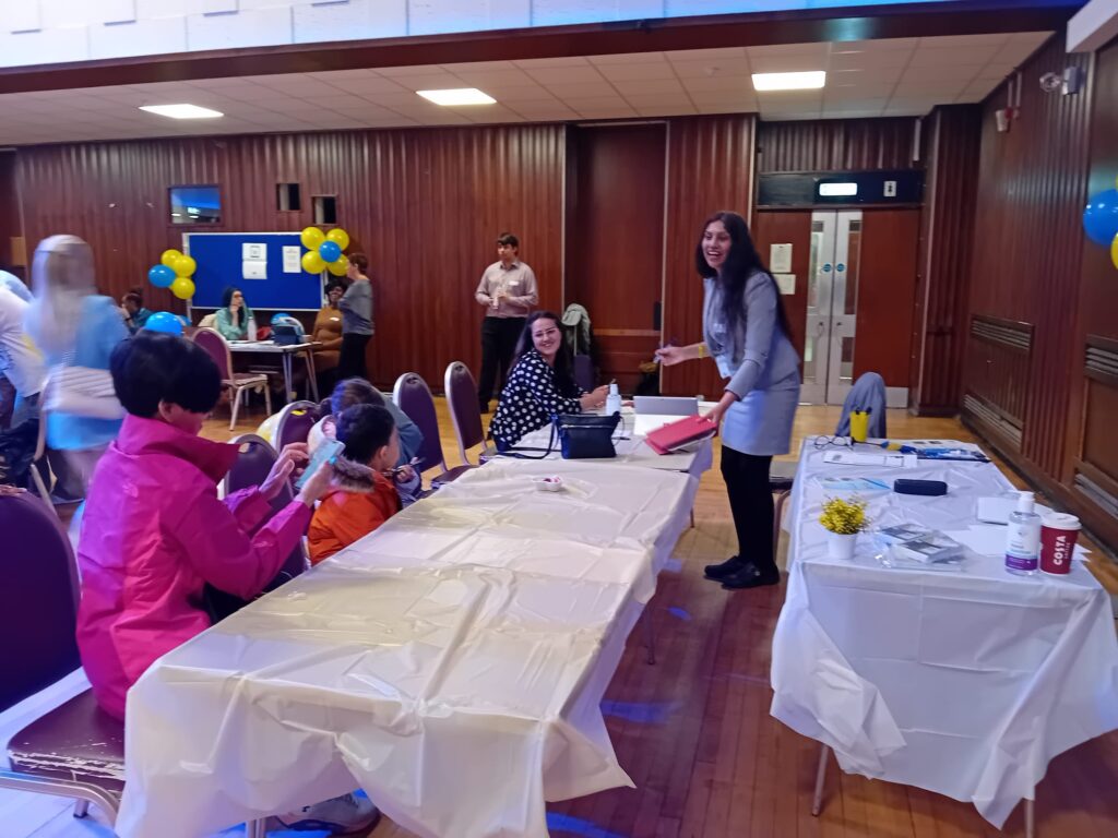 A group of adults and children sitting and standing around tables talking to each other, engaged in a workshop