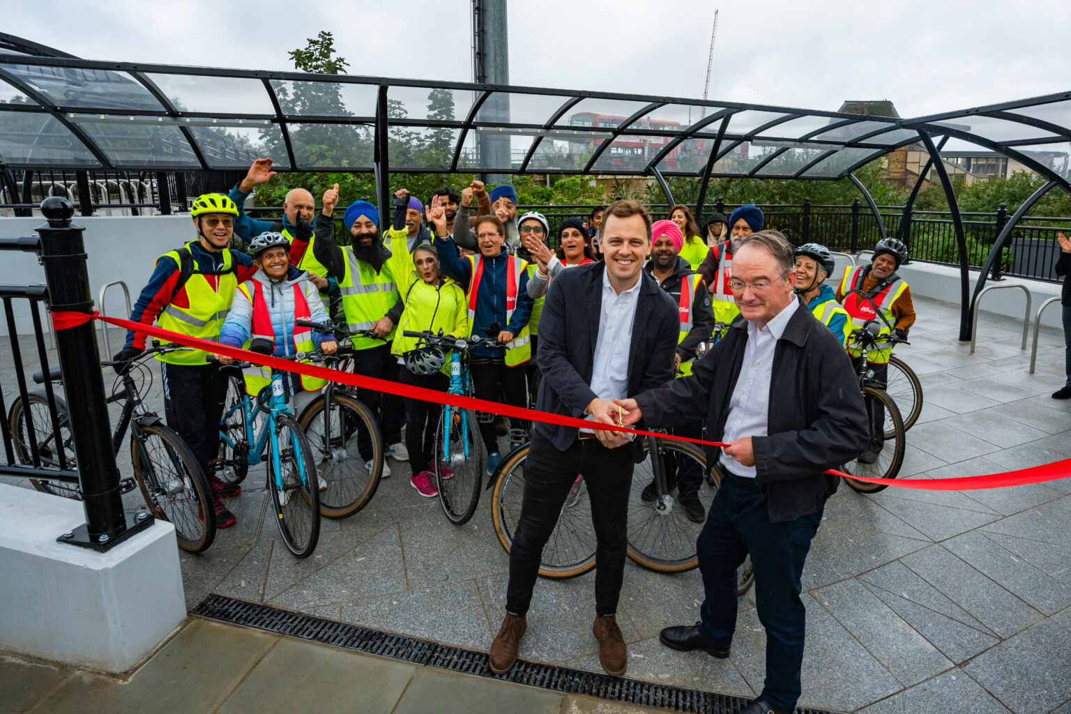 Leader of Ealing Council Councillor Peter Mason and Cabinet Member for Climate Action Councillor Paul Driscoll cutting a red ribbon to mark the opening of a new bike hub by Southall station.