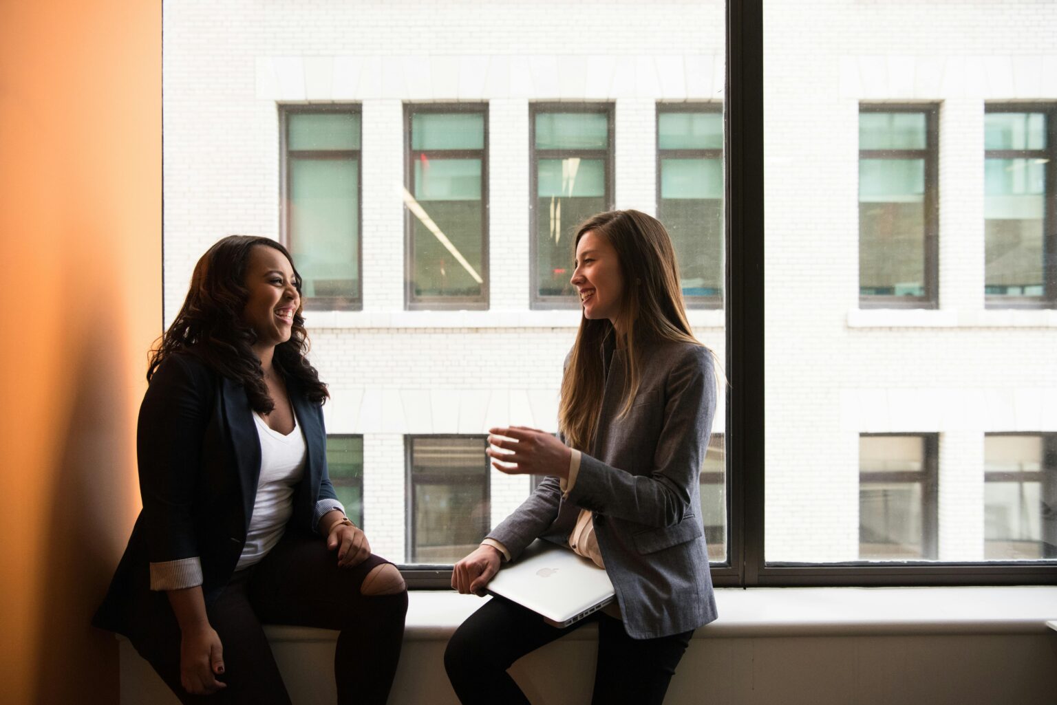 Woman in grey formal coat sitting near black full-glass panel Window. Secure your next job with West London Alliance Skills and Work Finder.