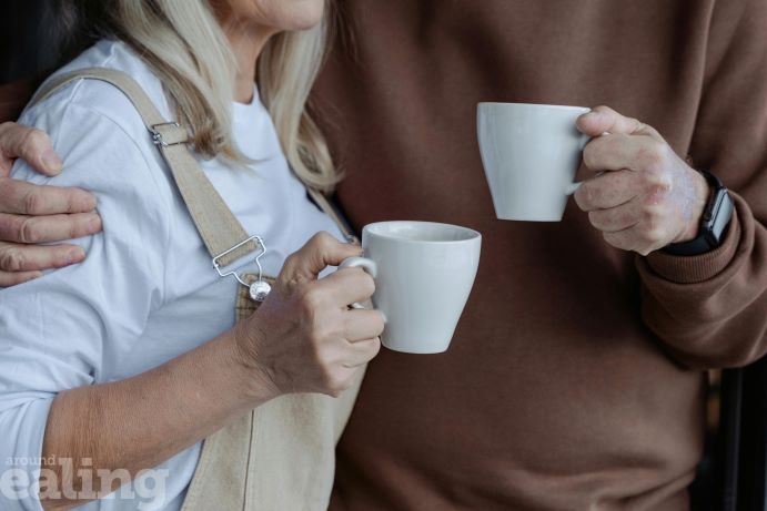 close up of man with arm round a woman, each holding a mug of tea