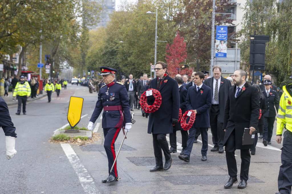 Group of men in formal attire march holding a wreath of poppy's on Remembrance Sunday 