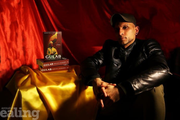 male author sitting next to stack of his new release book Gulab