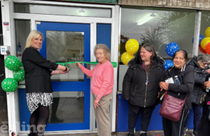 A woman stands beside three local women as she cuts a ceremonial ribbon at a doorway, marking the official opening of a new community space.