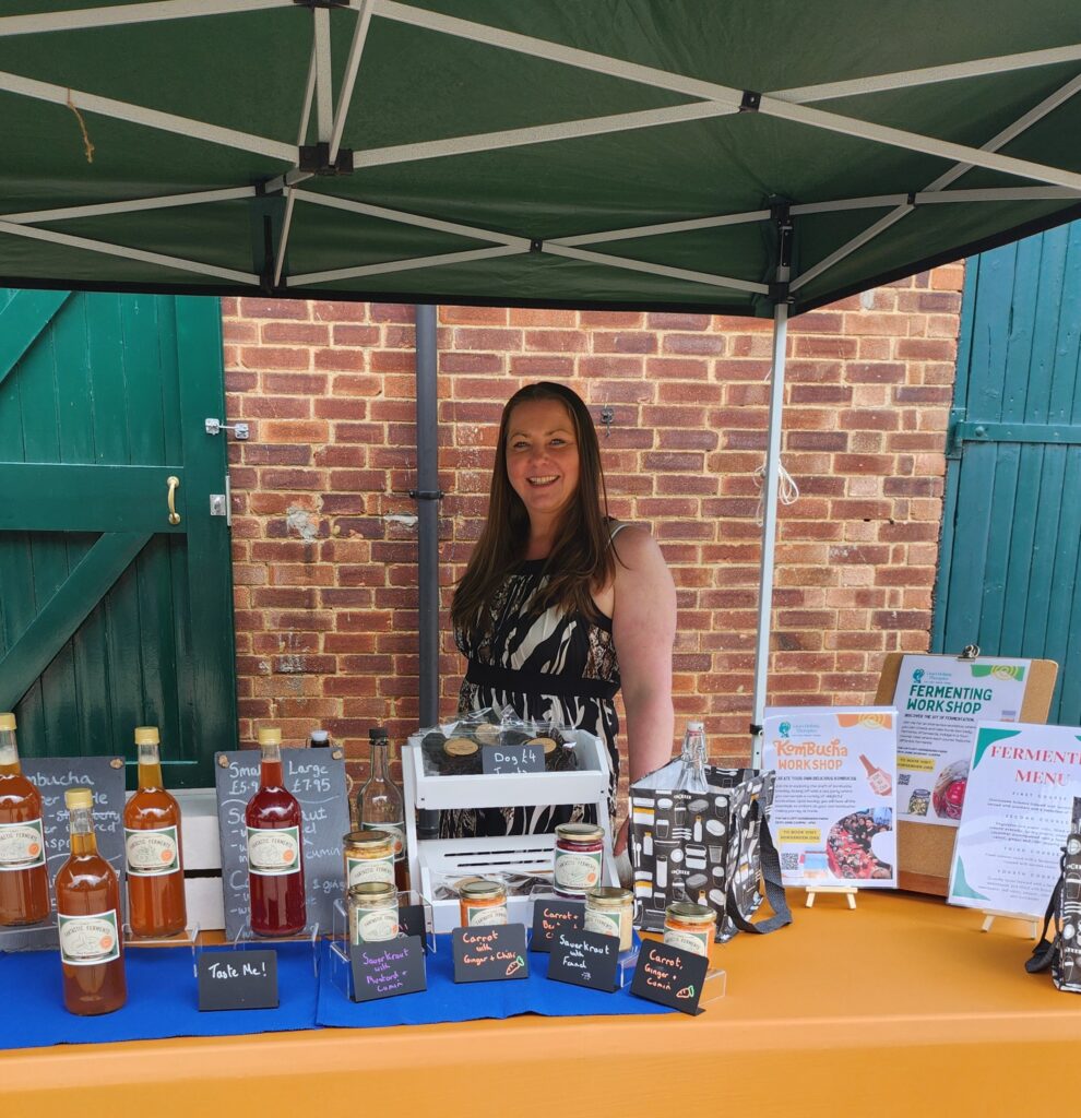 Woman standing behind table smiling with products from business on the table