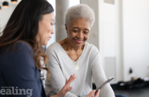 Young woman sits with an elderly woman while holding a tablet. Over 100 older people received pension credit. thanks to Ealing Council.