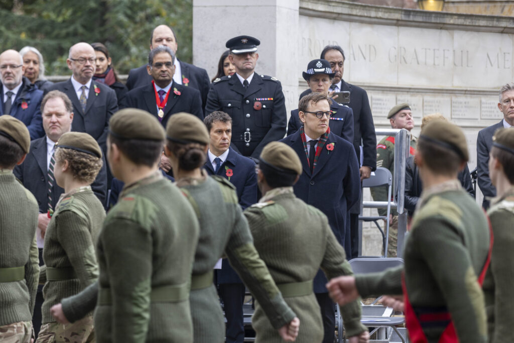 Group of armed forces personnel and Ealing Council staff stand and watch Remembrance Sunday ceremony 