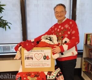 Councillor Paul Driscoll wearing a Christmas jumper, with his hands on a collection box for jumpers