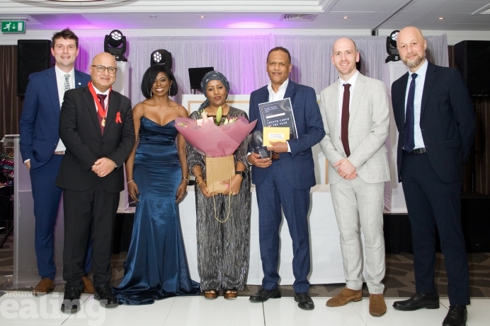 Group of people on a stage smiling at the camera, two (a man and a woman) are holding an award and smiling