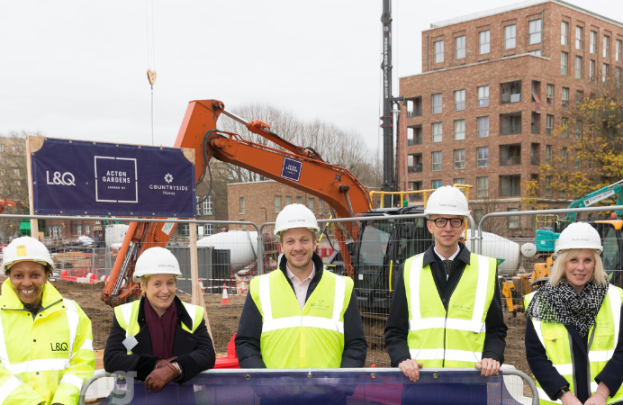 At the construction site of a South Acton estate, 5 adults wear high-visibility jackets and construction helmets, stood in a line, posing for a photo.