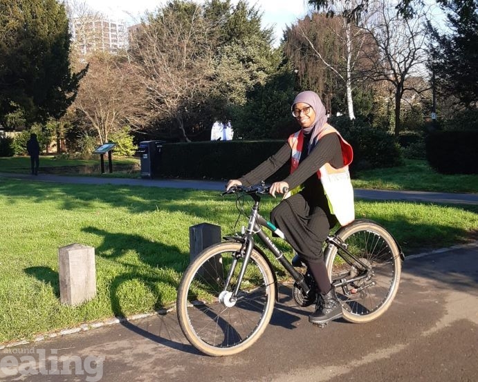 Huda riding her bike along a path in a park.