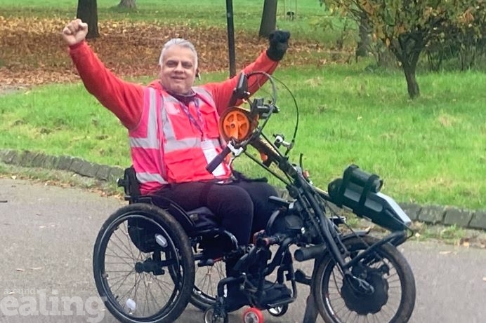 Kudlip with his arms up wheeling along on his hand bike