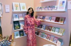 Hanaa, lady in pink dress standing in front of shelves with stationery at Creative Enterprise Zone