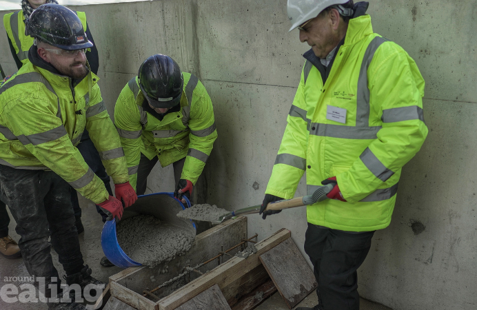 Three men in yellow high-vis jackets mix and apply cement at a construction site at Merrick Place.