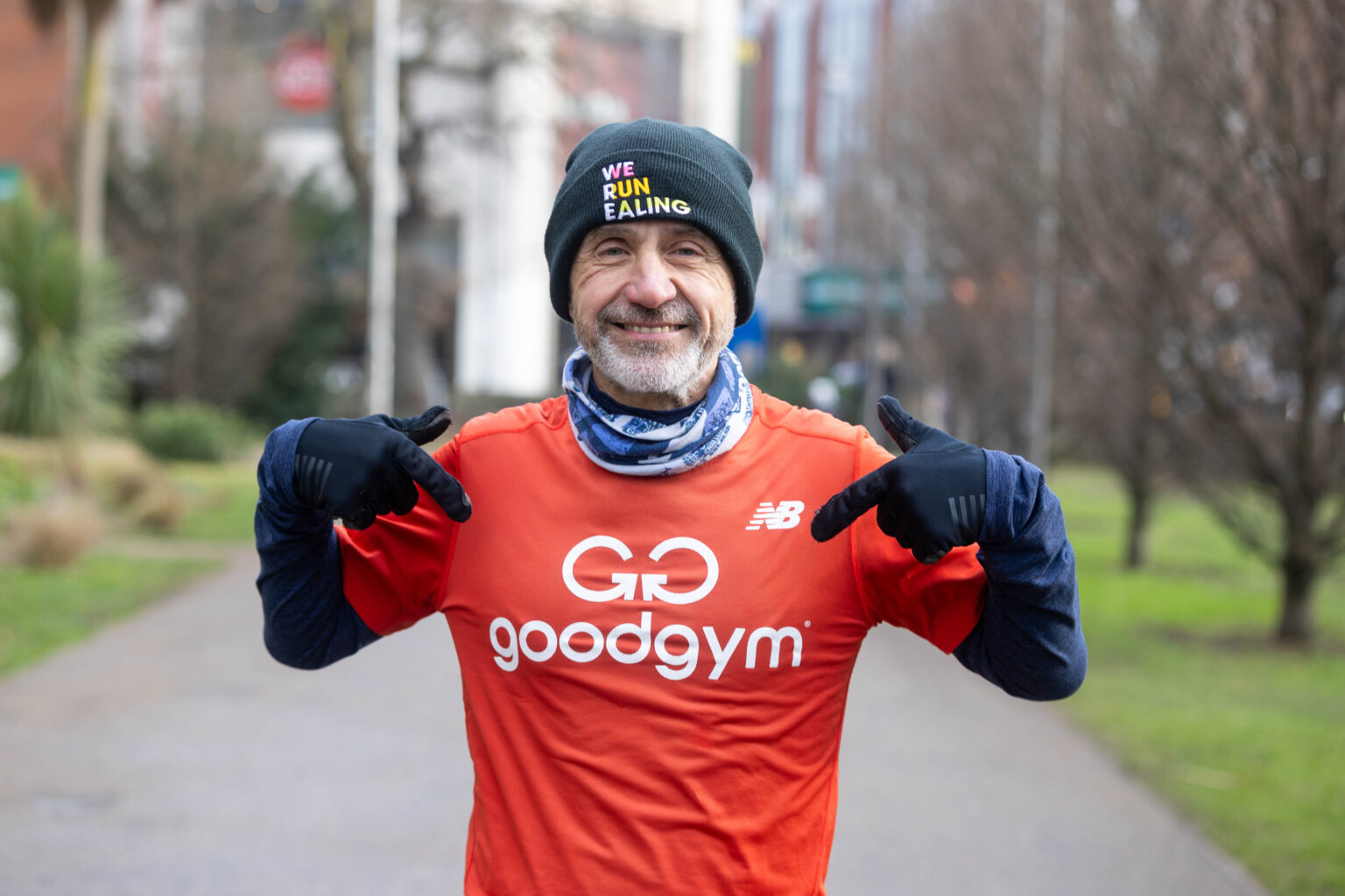 smiling man in running gear pointing to the Good Gym logo on his top