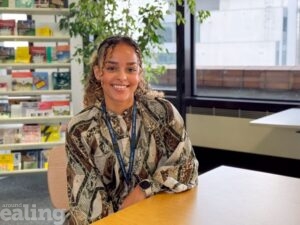 woman, smiling, sitting at a table with bookshelf in background