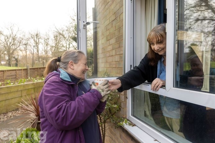 Gardening volunteer Cheryl having a cup of tea passed by a resident through an open window