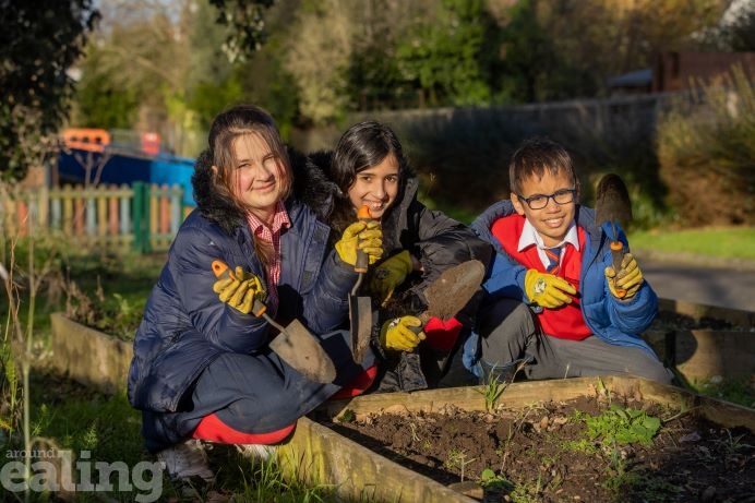 3 children kneeling at a flower bed outdoors, holding gardening equipment