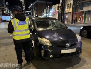 A Greener Ealing enforcement officer standing next to a car that's illegally parked.