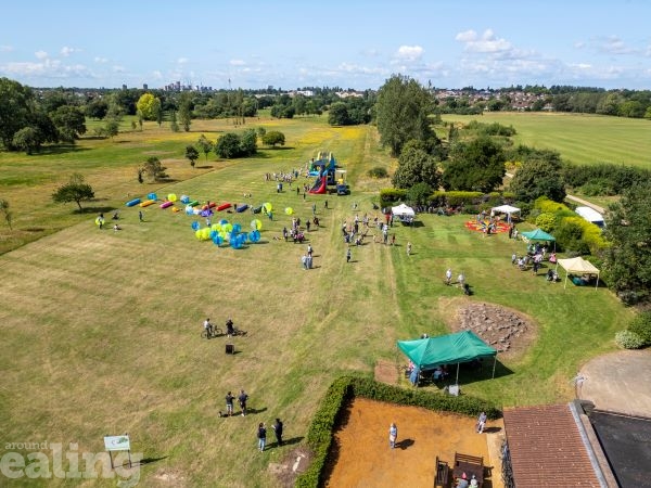 An aerial view of Pear Tree Park on a sunny day. There is a large expanse of grass and trees with a gazebo in the field. There are also small groups of people.